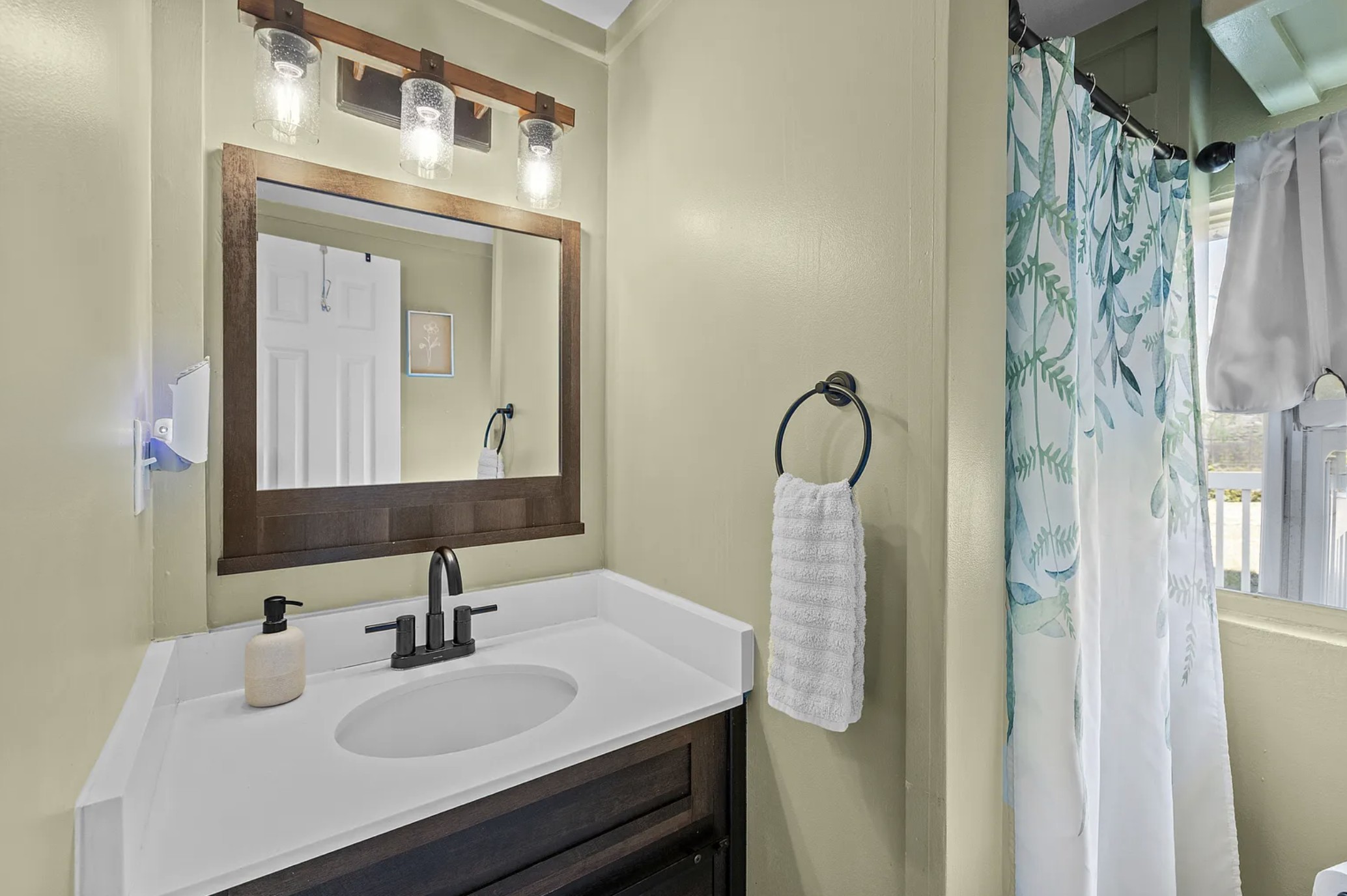 Bathroom vanity with dark wood mirror frame and sconce lighting