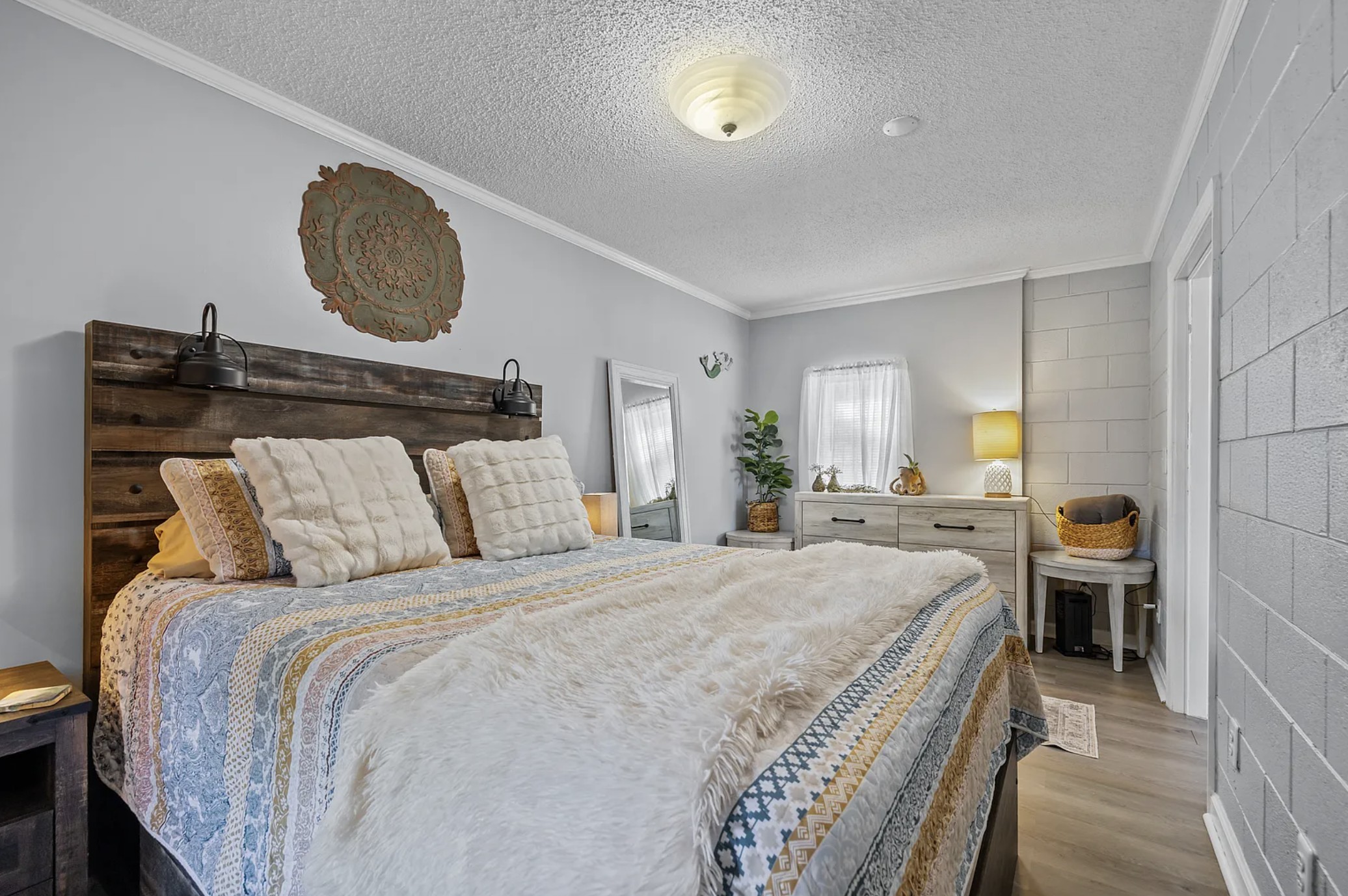 Queen bedroom with rustic wood headboard, sconce lighting, and medallion wall decor